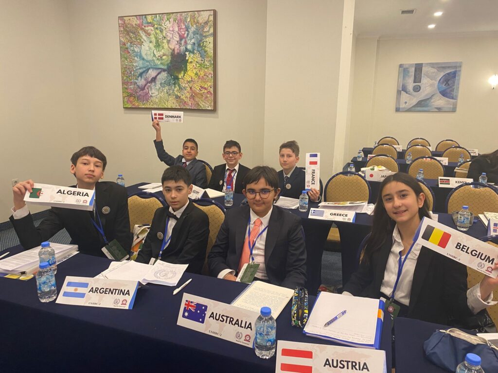 JMUN konferansında ülke tabelalarıyla oturan Maya Okulları öğrencileri