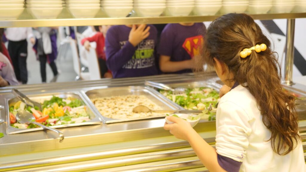 Öğrenci yemekhanede salata barından kendi tabağını hazırlıyor